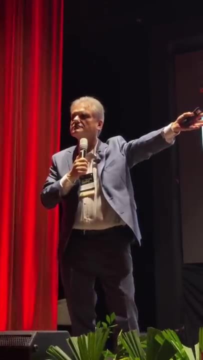 Edgar Madruga com microfone, gesticulando durante uma palestra