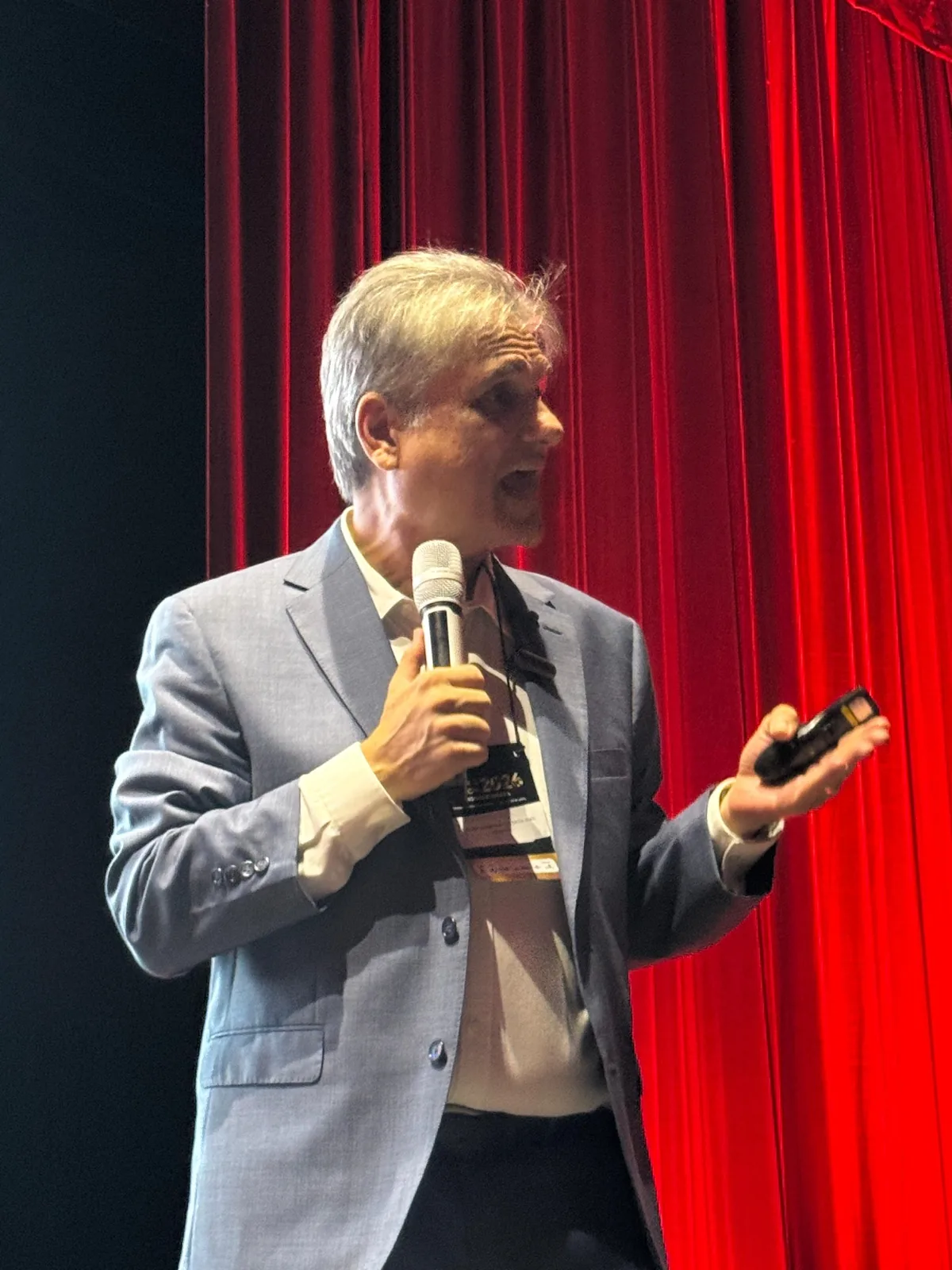 Edgar Madruga palestrando com microfone, diante de cortina vermelha