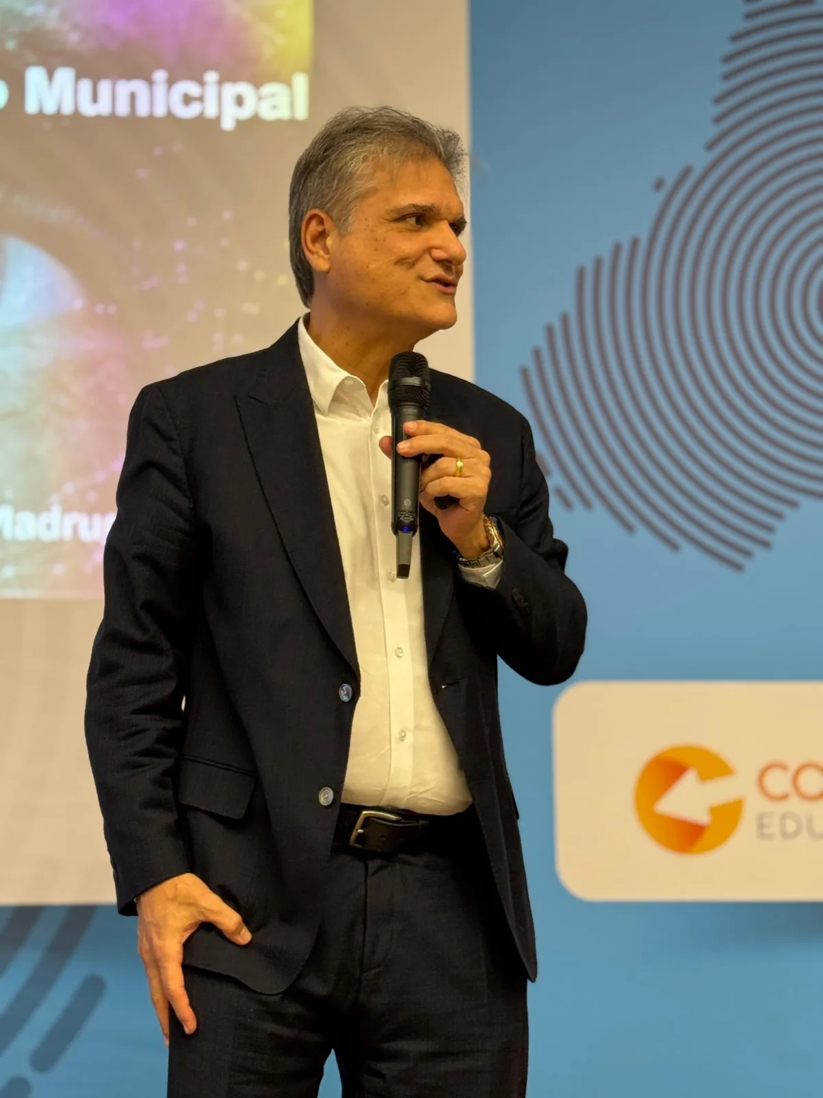 Edgar Madruga com microfone diante de um telão